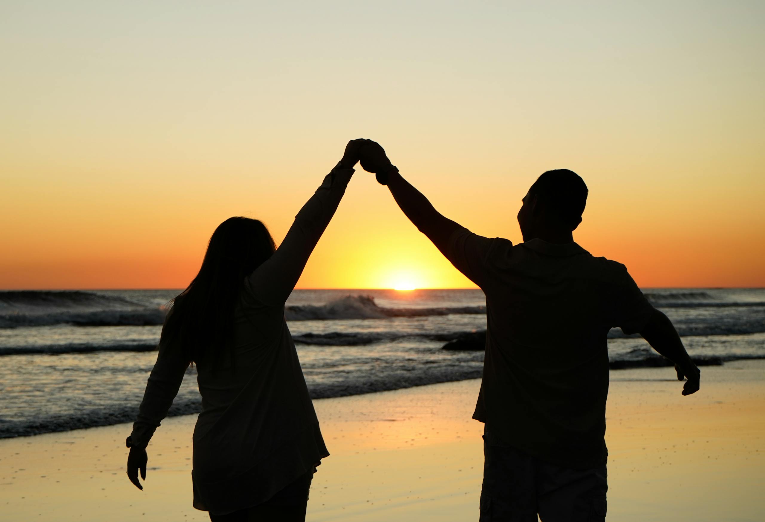 A couple in silhouette shares a romantic moment at the beach during a stunning sunset.