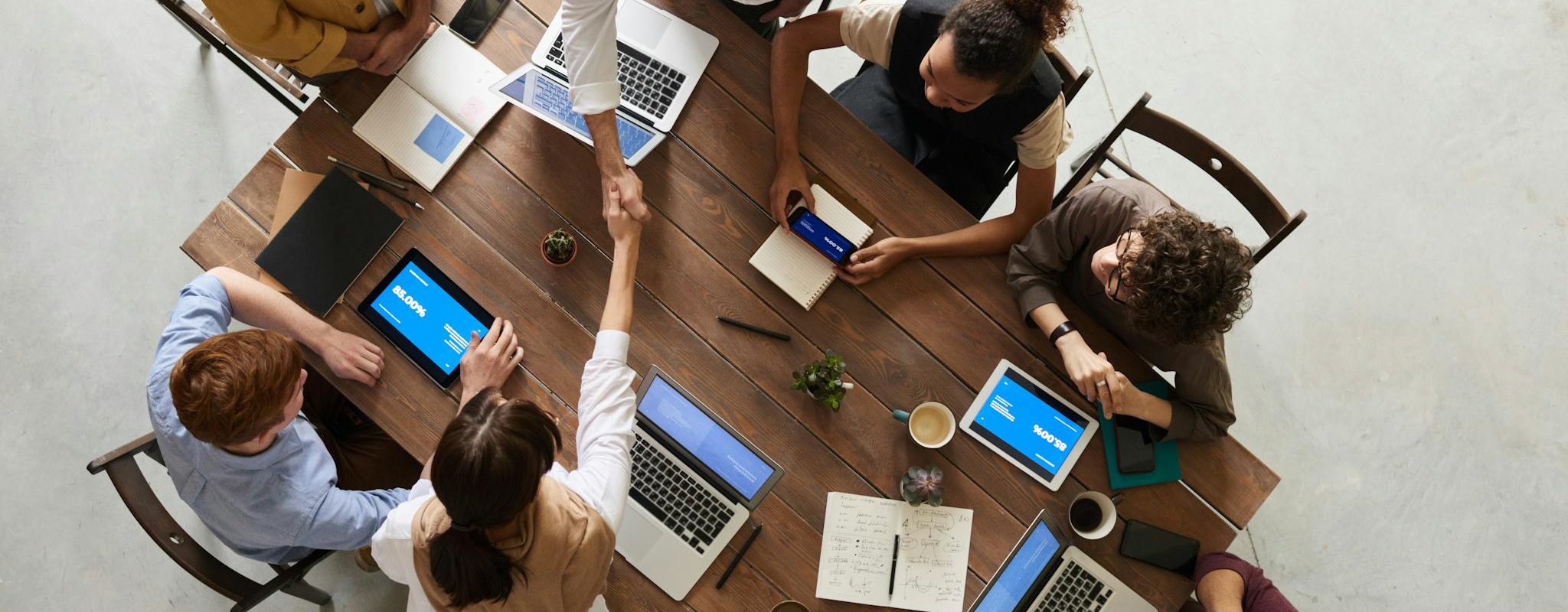 Top view of a diverse team collaborating in an office setting with laptops and tablets, promoting cooperation.