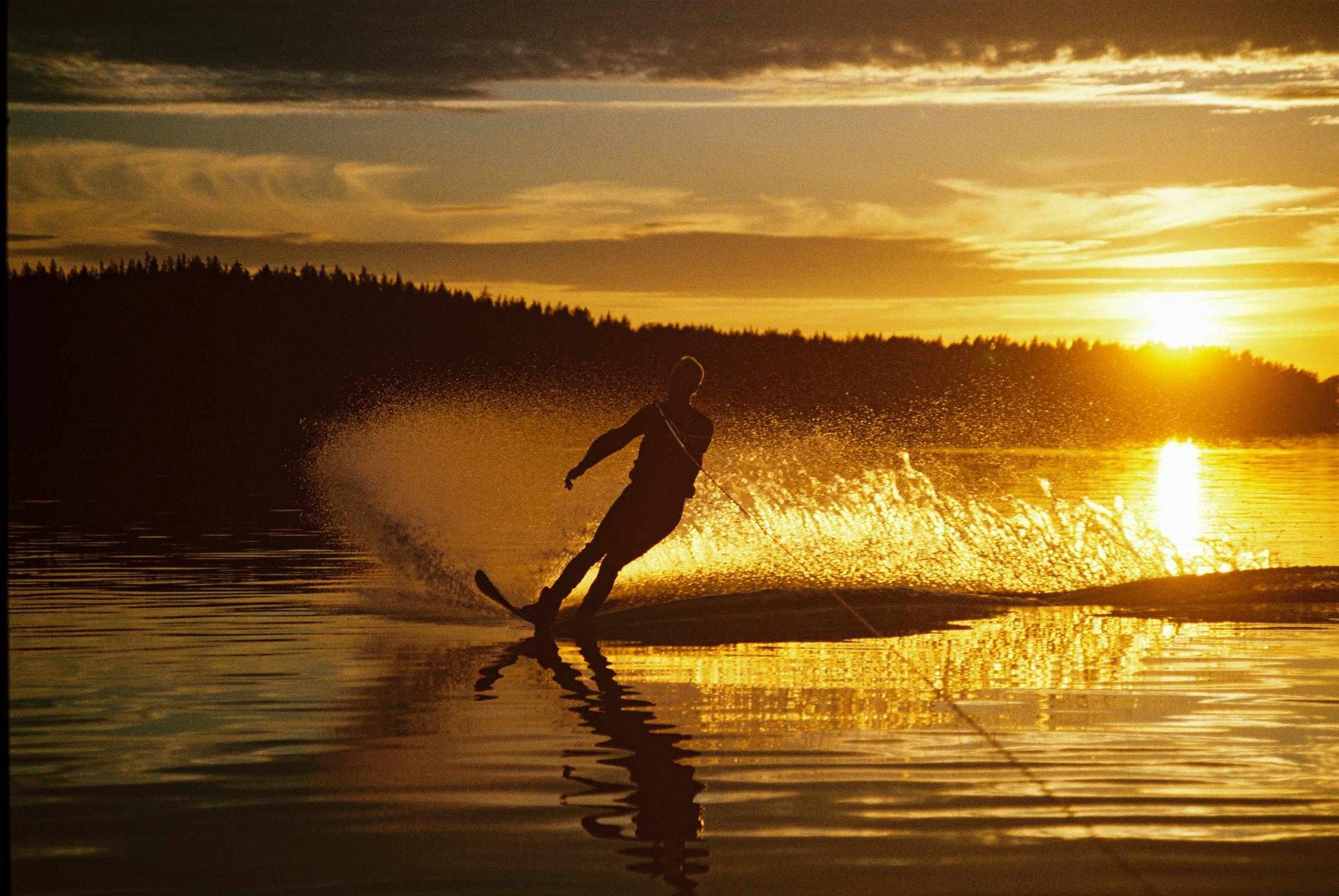 A person waterskiing on a tranquil lake during a vibrant sunset.