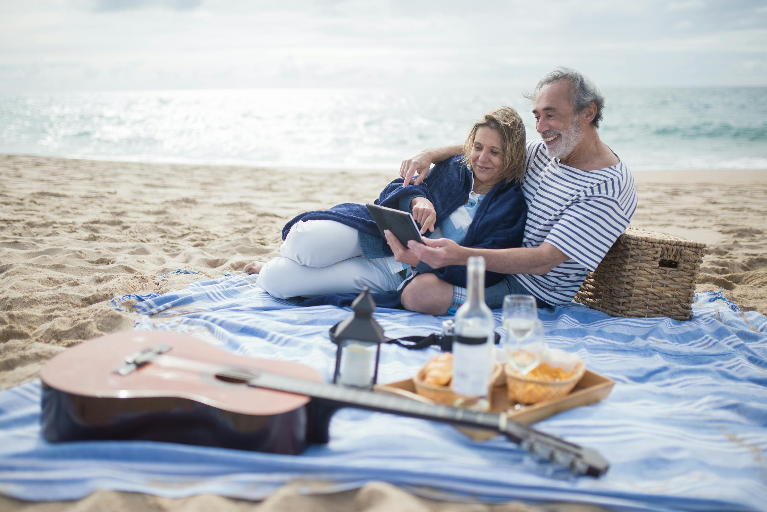 A happy senior couple enjoys a beach picnic in Portugal, embracing leisure and relaxation.