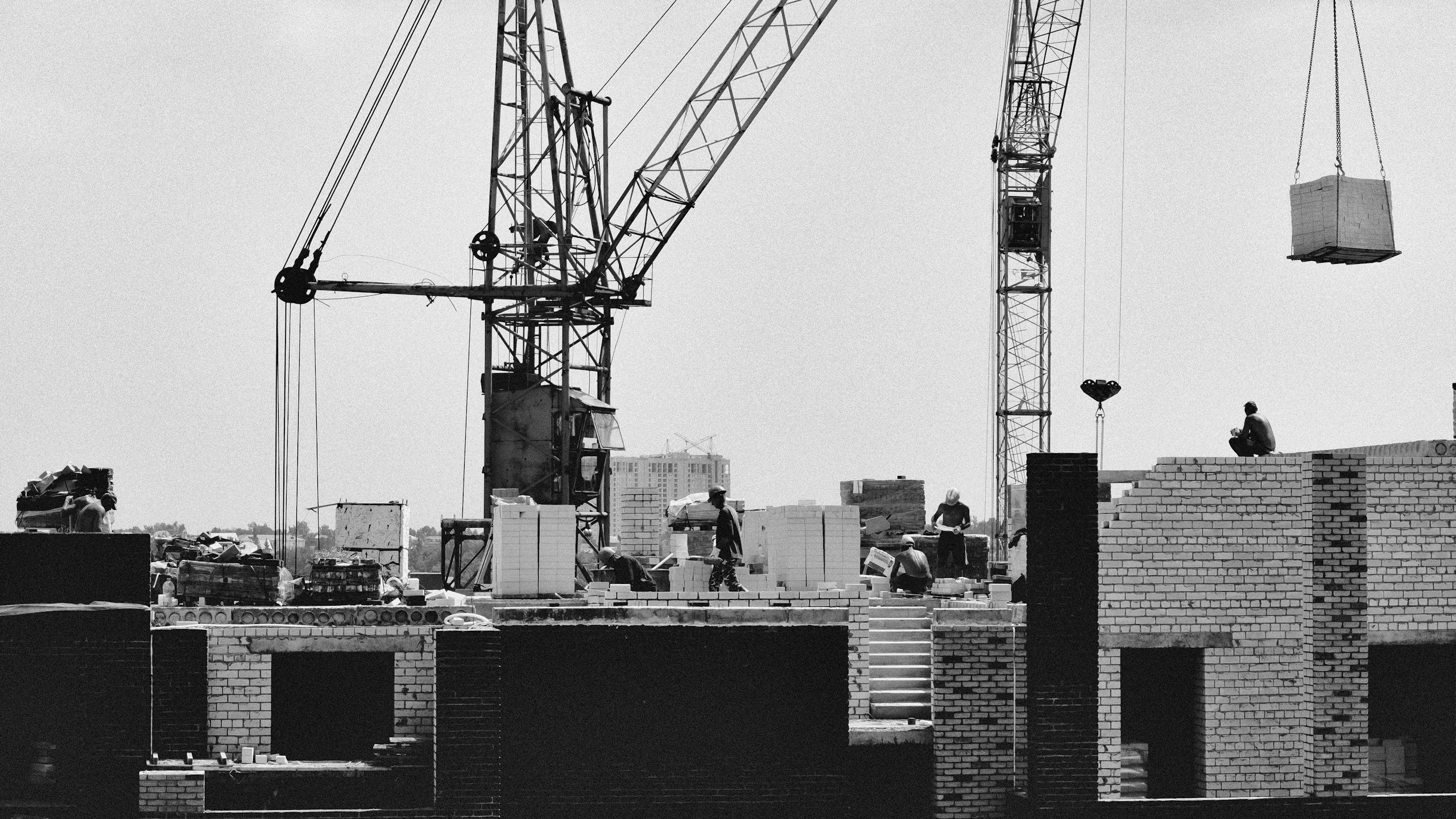Black and white image of a construction site with cranes and workers, emphasizing urban industrial development.