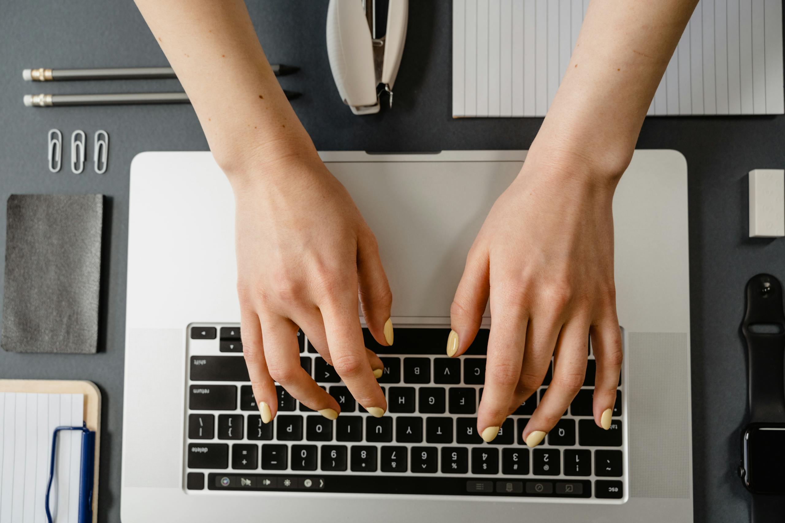 Close-up of woman's hands with manicured nails typing on a laptop.
